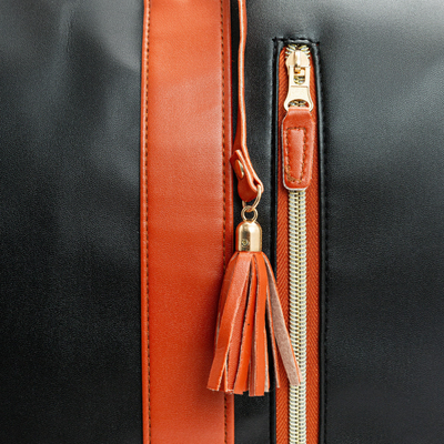 Gros plan d'un sac à main en cuir noir avec fermeture éclair dorée, bande et pompon en cuir marron. Accessoire de mode élégant et tendance.