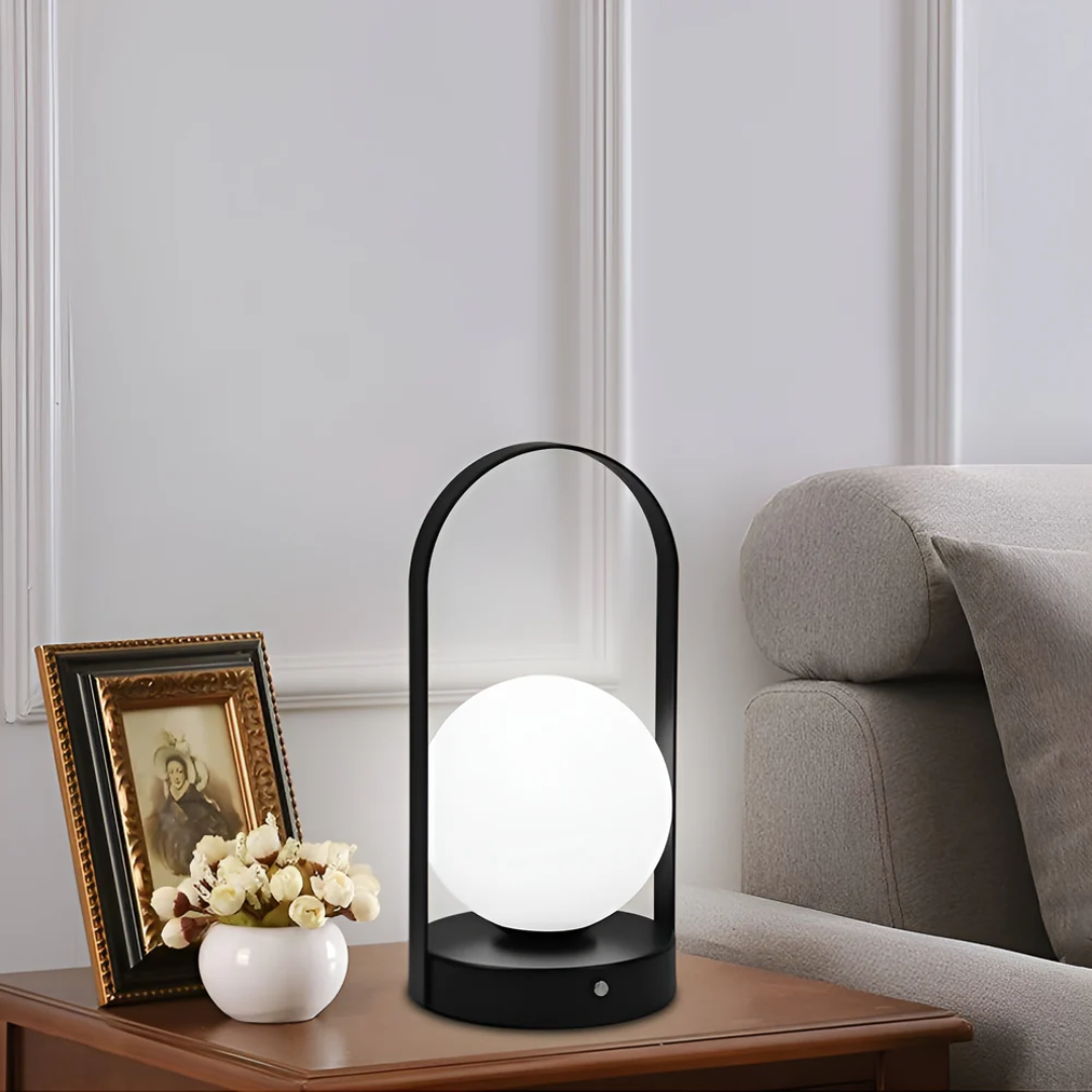 Lampe de table moderne noire avec globe lumineux sur table en bois, à côté d'un vase de fleurs et d'un cadre photo, dans un salon élégant.