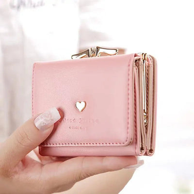 Portefeuille rose en cuir avec fermoir doré, motif cœur, tenu par une main féminine. Accessoire mode élégant et tendance pour femmes.