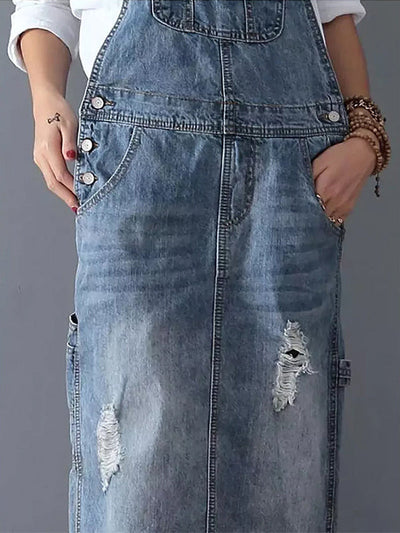 Robe salopette en jean bleu délavé avec poches, boutons argentés et détails déchirés. Mode décontractée, tendance denim, style urbain.