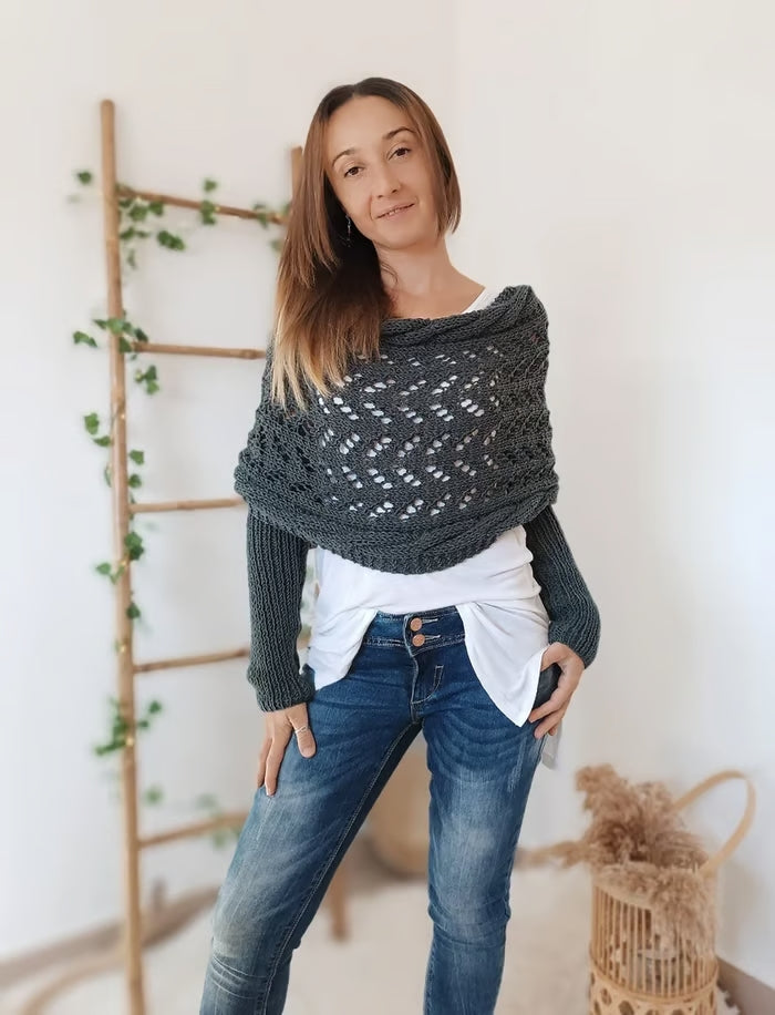 Femme portant un pull tricoté gris, posant devant une échelle en bois décorée de plantes. Mode automne-hiver, style décontracté, intérieur moderne.