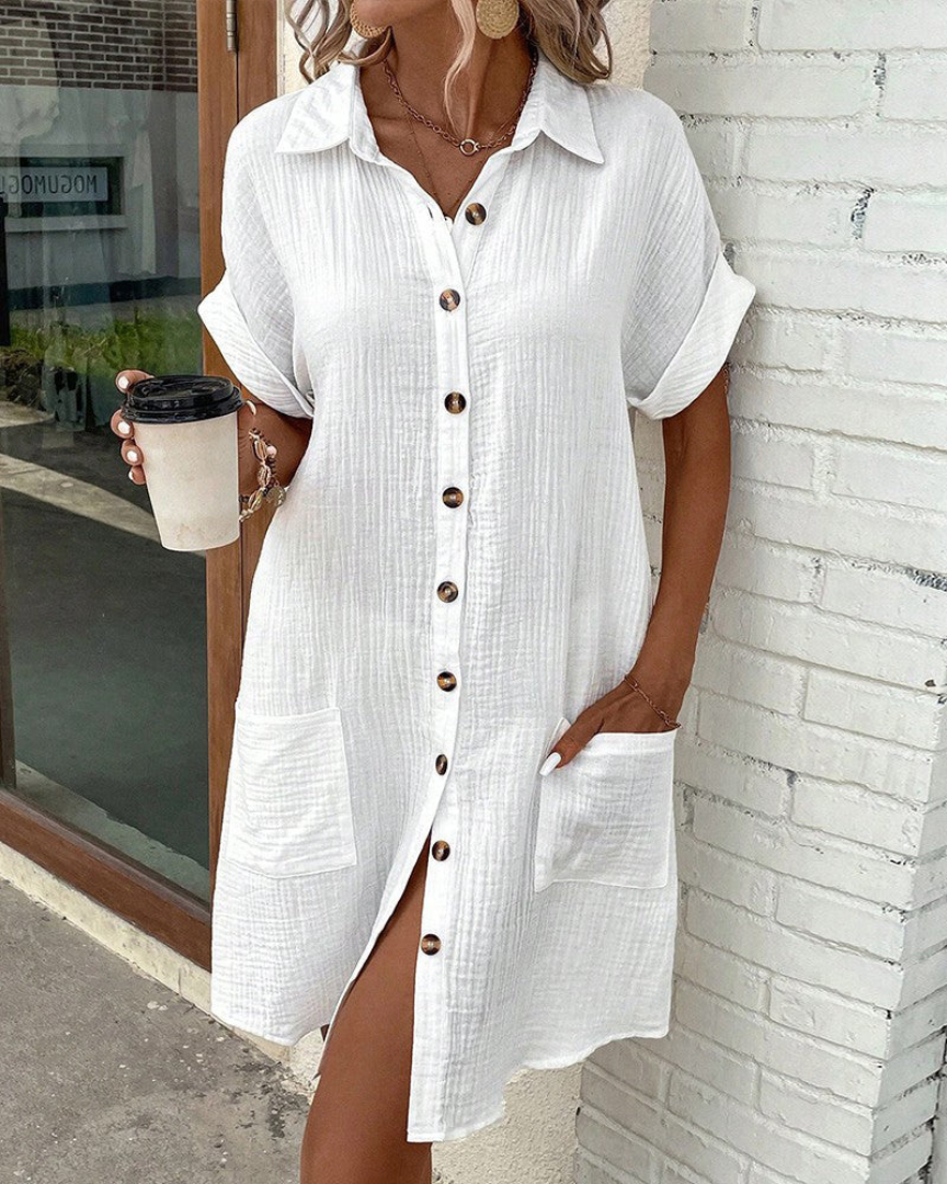 Robe chemise blanche en lin avec boutons en bois, manches courtes retroussées, poches avant, tenue d'été décontractée, femme tenant un café.