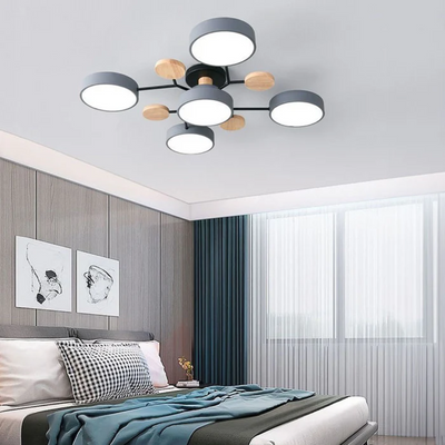 Plafonnier moderne à LED avec abat-jours circulaires noirs et détails en bois, installé dans une chambre élégante avec lit et décor minimaliste.