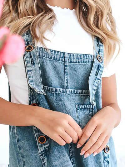 Femme portant une salopette en jean bleu avec un t-shirt blanc, cheveux blonds ondulés. Mode décontractée, tendance denim, style estival.