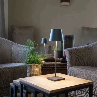 Lampe de table moderne sur une table en bois entre deux fauteuils élégants, plante verte en pot, ambiance salon cosy et design.