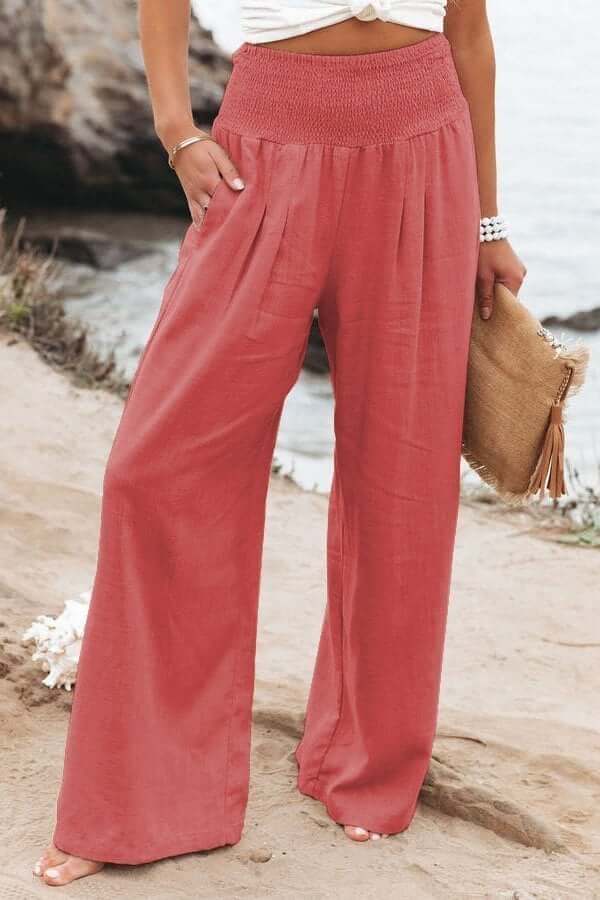 Pantalon large rose en lin pour femme, style décontracté, bord de mer. Mode estivale, tenue confortable, accessoire sac en paille.