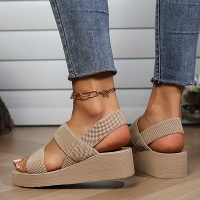 Sandales compensées beiges en maille, portées avec un jean ajusté, sur fond de plancher en bois. Mode estivale, chaussures tendance femme.