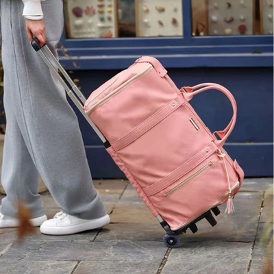 Personne tirant un sac de voyage à roulettes rose, élégant et spacieux, sur un trottoir. Sac en cuir avec poignées et fermetures éclair dorées.