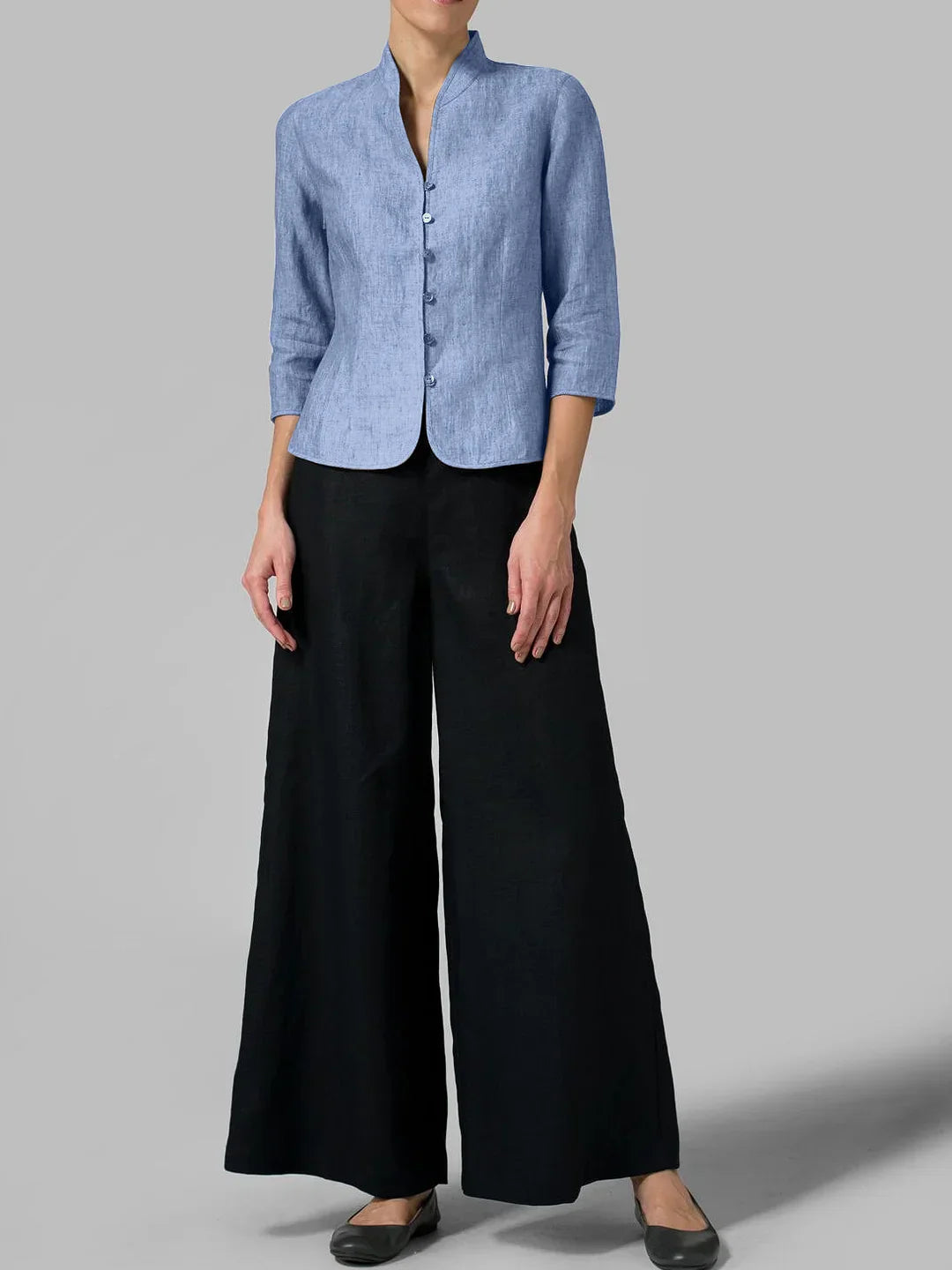 Femme portant une veste bleue en lin à manches trois-quarts et un pantalon large noir, mode élégante et décontractée, fond gris.