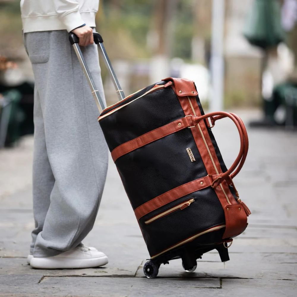 Personne tirant un sac de voyage à roulettes noir et marron, tenue décontractée, extérieur urbain. Sac en cuir, idéal pour voyages et week-ends.