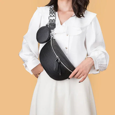 Femme portant un sac banane noir en cuir avec sangle à motifs géométriques, sur fond beige. Mode, accessoires tendance, style chic.