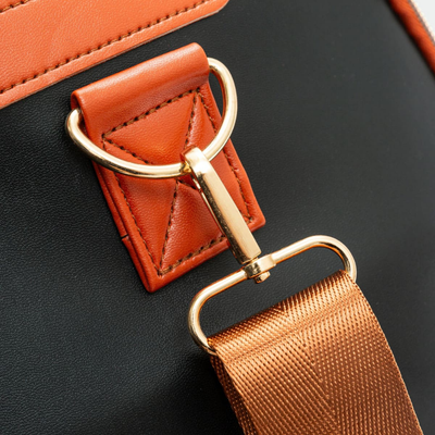 Boucle dorée sur sac à main en cuir noir et orange, design élégant, accessoire de mode tendance, détail de couture et sangle en tissu.