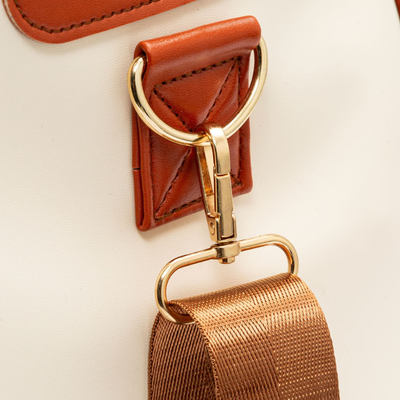 Boucle dorée sur sac à main en cuir blanc et marron, avec sangle en tissu marron. Accessoire de mode élégant et tendance.