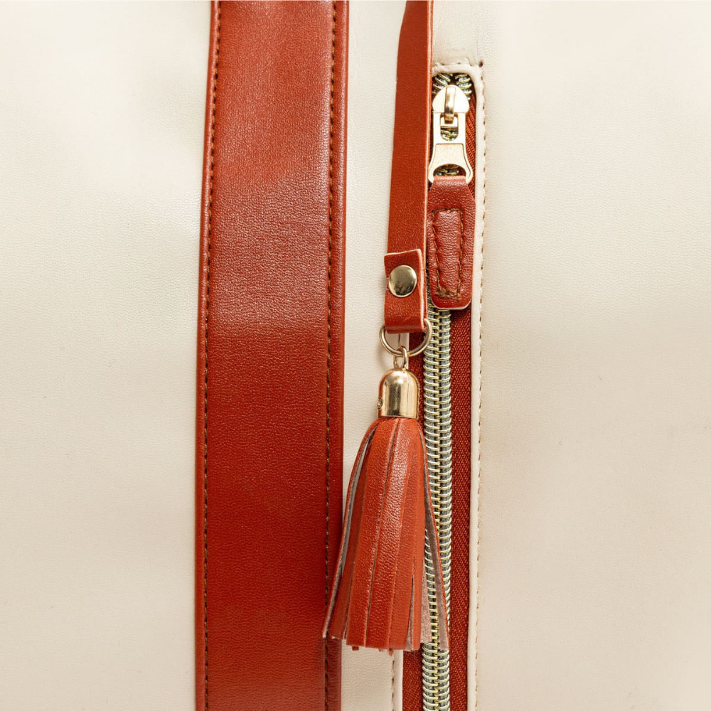 Gros plan sur un sac à main en cuir beige avec fermeture éclair dorée et pompon en cuir marron. Accessoire de mode élégant et tendance.