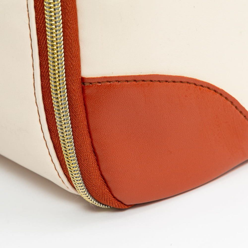 Sac en cuir blanc avec coin renforcé en cuir orange et fermeture éclair dorée. Accessoire de mode élégant et moderne.