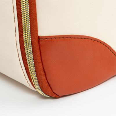 Sac en cuir blanc avec coin renforcé en cuir orange et fermeture éclair dorée. Accessoire de mode élégant et moderne.