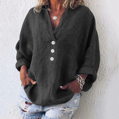 Femme portant une chemise noire ample avec boutons blancs, manches retroussées, associée à un jean déchiré. Mode décontractée, tendance et élégante.