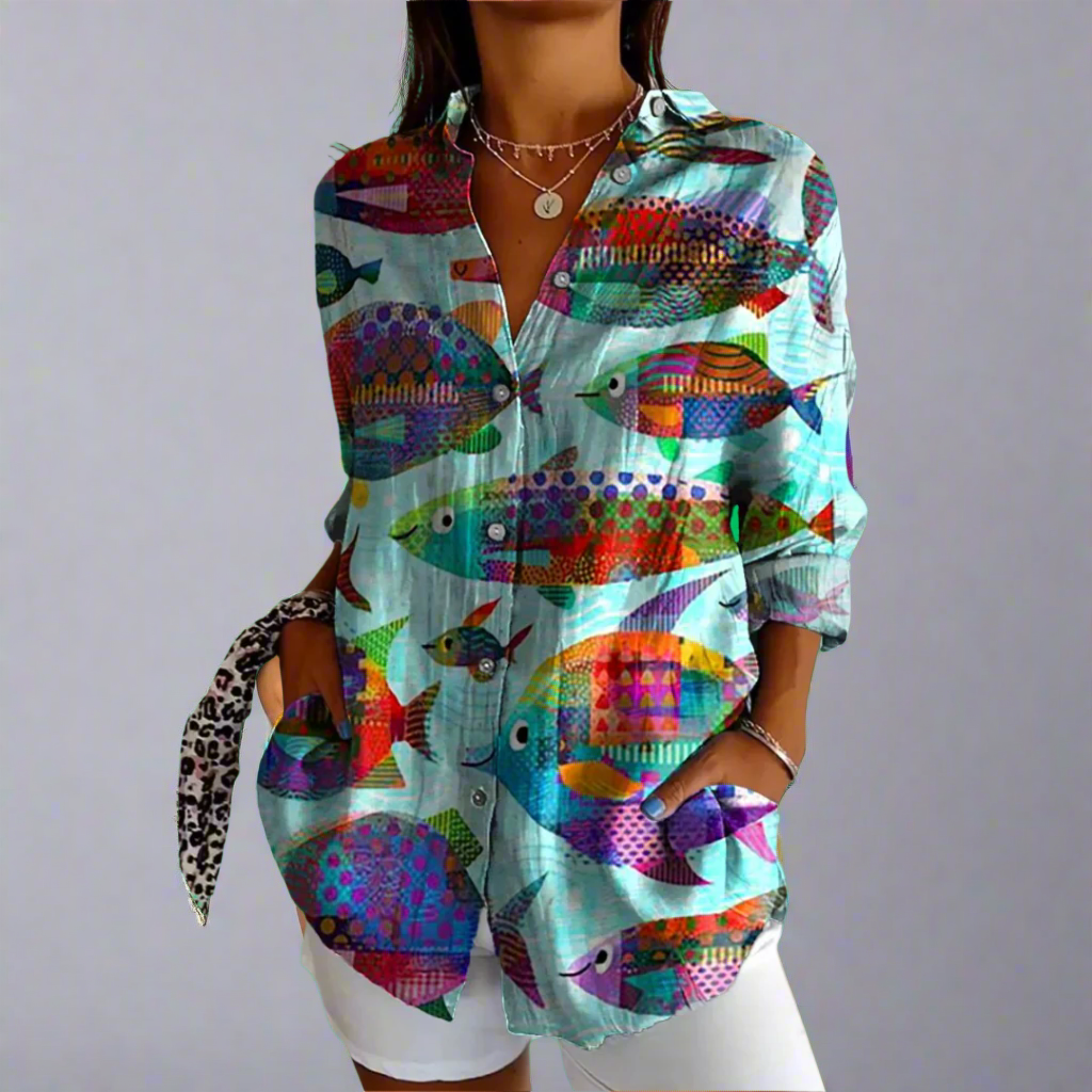 Chemise femme colorée à motifs de poissons, manches longues, col ouvert, portée avec un collier et un short blanc. Mode tendance, style décontracté.