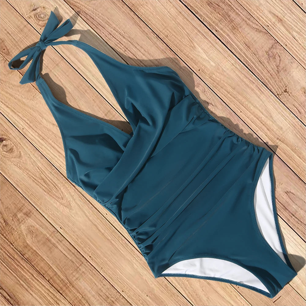 Maillot de bain une pièce bleu canard sur plancher en bois, design dos nu avec nœud, style élégant et moderne pour plage ou piscine.