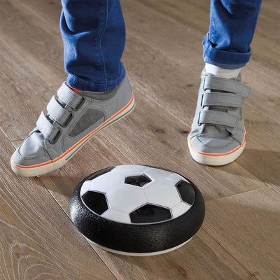 Enfant jouant avec un ballon de football flottant sur parquet, chaussures grises à scratch, jouet interactif intérieur, jeu enfant innovant.