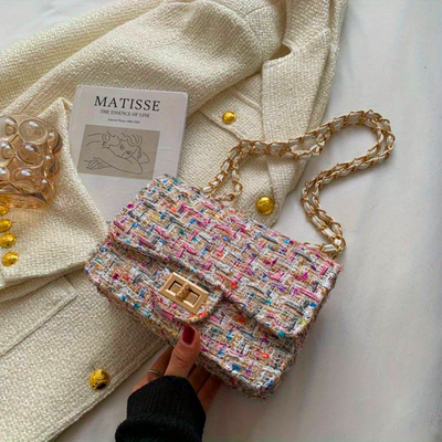 Sac à main en tweed multicolore avec chaîne dorée sur manteau blanc, livre "Matisse" et décorations dorées. Accessoire mode élégant et tendance.