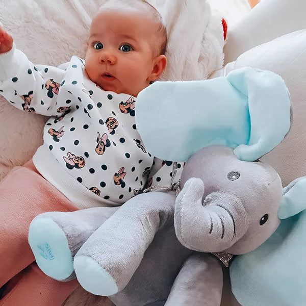 Bébé allongé sur un coussin avec un pull à motifs, à côté d'une peluche éléphant grise et bleue. Jouet doux, enfant, confort.