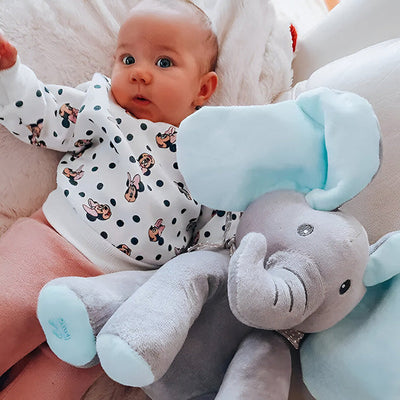 Bébé allongé sur un coussin avec un pull à motifs, à côté d'une peluche éléphant grise et bleue. Jouet doux, enfant, confort.