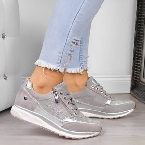 Chaussures de sport grises pour femme avec détails métalliques, portées avec un jean déchiré clair. Mode féminine, baskets tendance, style décontracté.