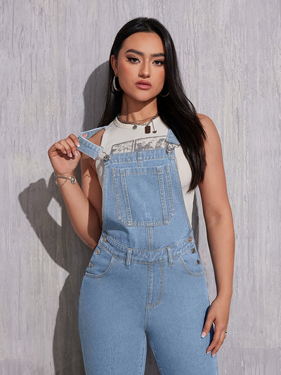 Femme portant une salopette en jean bleu clair, t-shirt blanc, posant devant un mur texturé. Mode décontractée, tendance denim, style urbain.