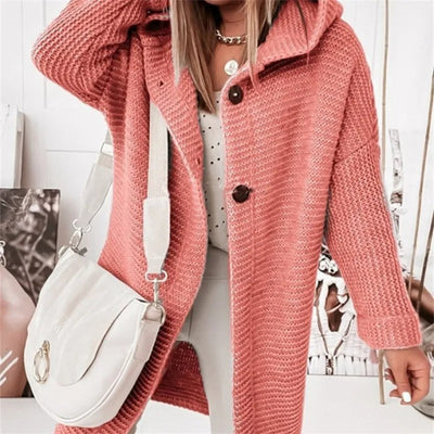 Femme portant un manteau en tricot rose avec capuche, sac à main blanc, collier doré, mode automne-hiver, style décontracté chic.