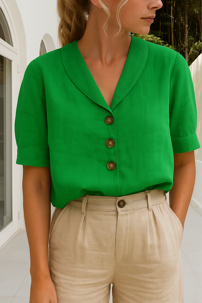 Femme portant une chemise verte à boutons marron et un pantalon beige, posant dans un intérieur moderne. Mode élégante, tenue estivale chic.
