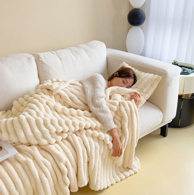 Femme endormie sur un canapé blanc, enveloppée dans une couverture en peluche beige. Décor moderne, ambiance cosy et détente à la maison.