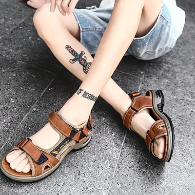 Sandales en cuir marron pour homme, portées avec un short en jean. Design confortable, idéal pour l'été. Tatouage visible sur la jambe.