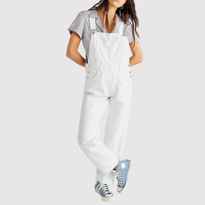 Femme portant une salopette blanche et une chemise à carreaux, baskets bleues. Mode décontractée, tenue tendance, style urbain.