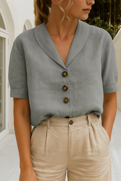 Femme portant une chemise grise élégante à boutons marron et un pantalon beige, posant dans un intérieur moderne et lumineux. Mode chic et minimaliste.