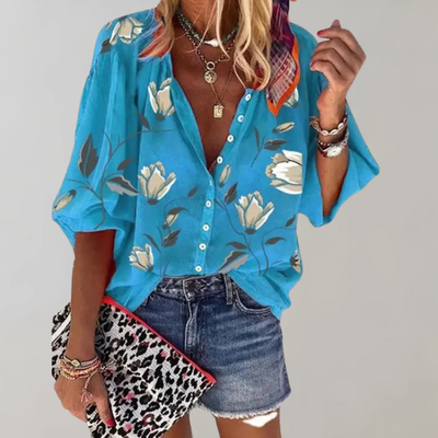 Chemisier bleu à fleurs blanches, manches amples, porté avec short en jean. Accessoires: pochette léopard, colliers, bracelets. Mode estivale chic.