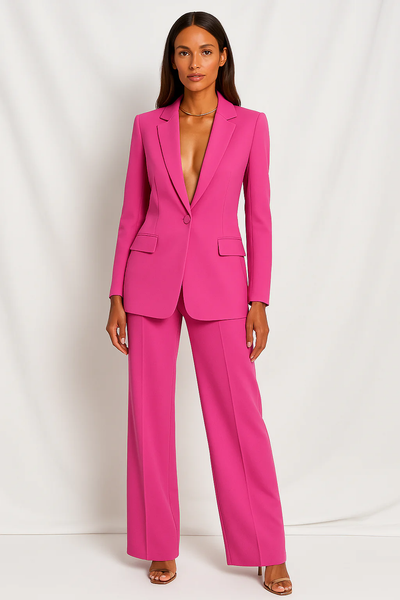 Femme portant un tailleur pantalon rose vif, veste ajustée, pantalon large, posant devant un fond blanc. Mode élégante, tendance, chic.