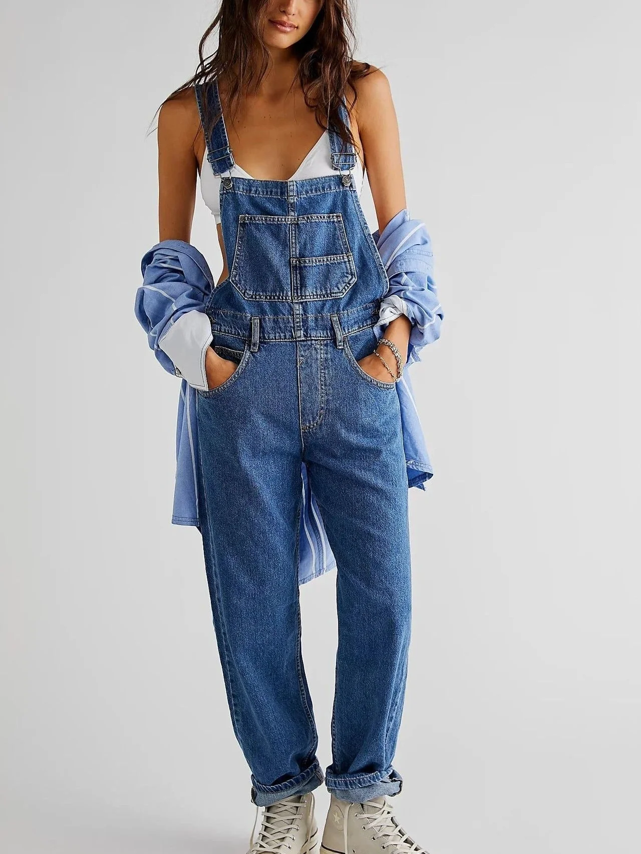 Femme portant une salopette en jean bleu avec une chemise bleue et des baskets blanches, mode décontractée, style urbain tendance.