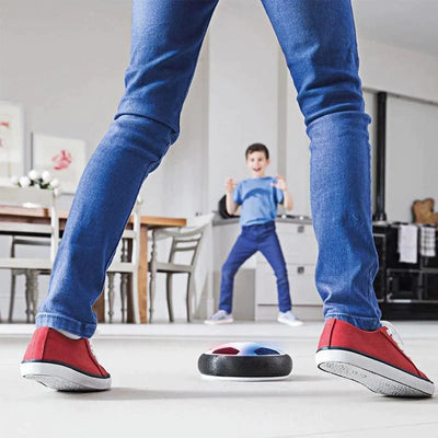 Enfant jouant au football d'intérieur avec un ballon flottant, chaussures rouges, salon moderne, jeu interactif, activité familiale amusante.