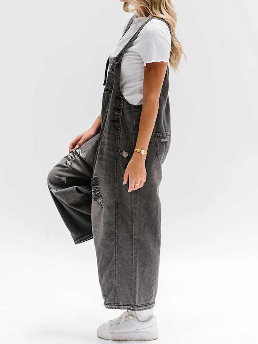 Femme portant une salopette en jean gris délavé avec t-shirt blanc, baskets blanches, posant de profil. Mode décontractée, tendance urbaine.