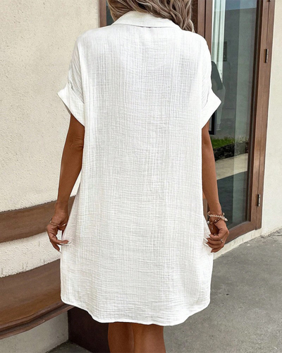 Robe chemise blanche en lin, manches courtes, style décontracté, femme de dos, devant une porte en bois, ambiance estivale et élégante.