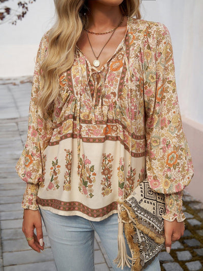 Femme portant un chemisier bohème à motifs floraux avec manches longues, collier doré, sac à main à franges, et jeans. Mode bohème chic tendance.
