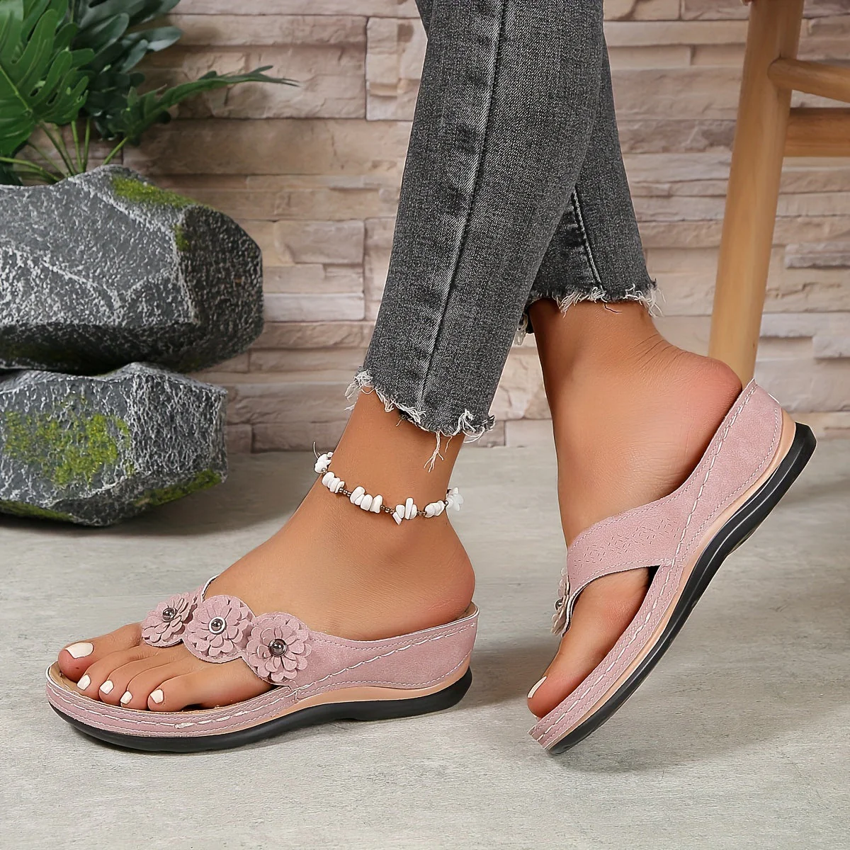 Sandales roses pour femmes avec fleurs décoratives, portées avec un jean gris effiloché. Accessoire de cheville en perles blanches.