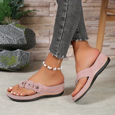 Sandales roses pour femmes avec fleurs décoratives, portées avec un jean gris effiloché. Accessoire de cheville en perles blanches.