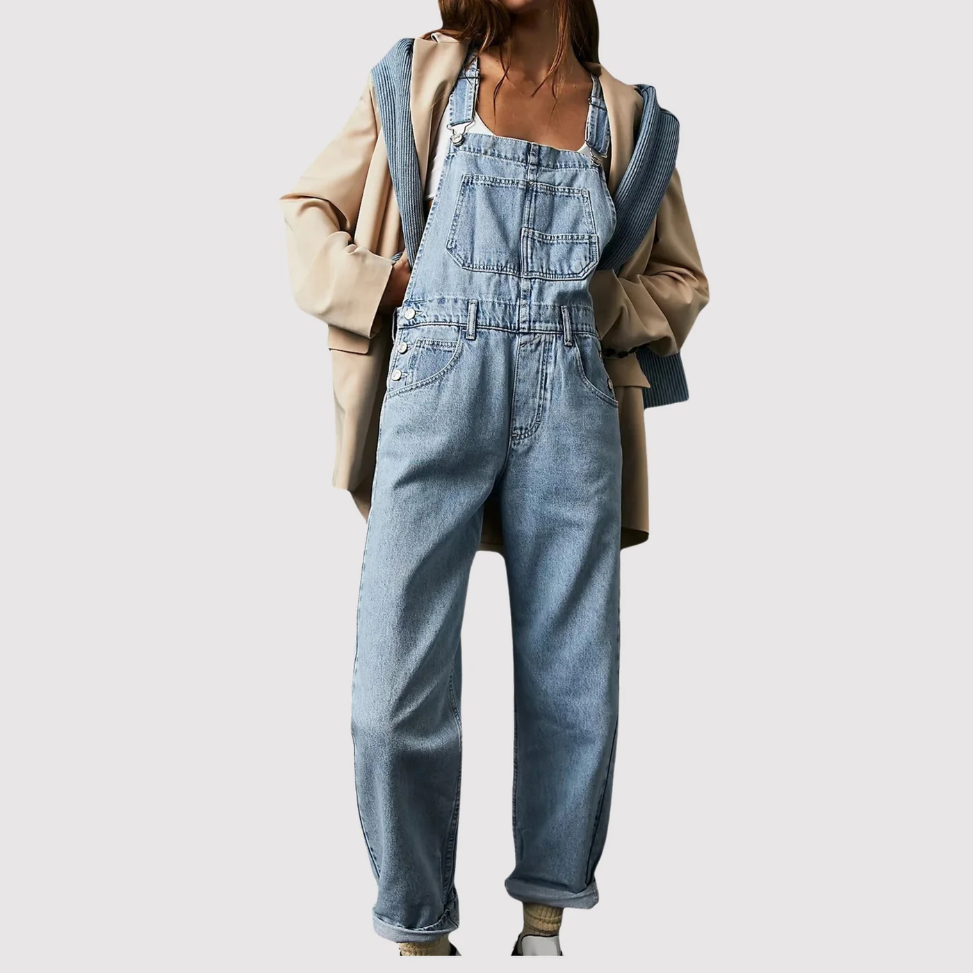 Salopette en jean bleu clair pour femme, style décontracté, avec veste beige et pull bleu noué, mode tendance automne-hiver.
