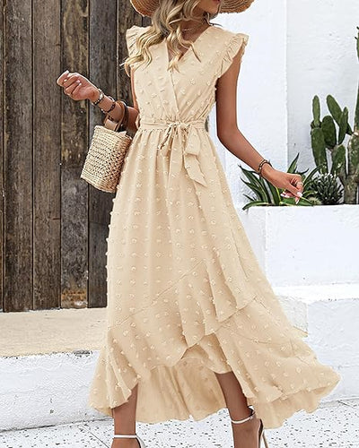Robe longue beige à volants, motifs à pois, portée par une femme avec un chapeau de paille et un sac en osier, devant un mur blanc et des plantes.