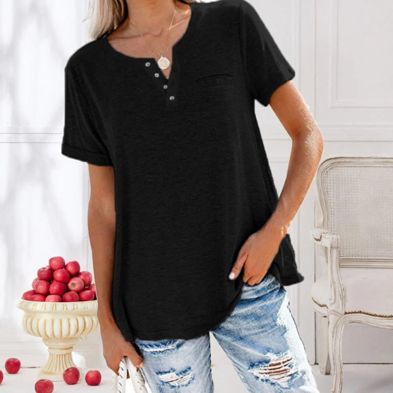 Femme portant un t-shirt noir à boutons, jeans déchirés, posant près d'un vase de pommes rouges dans un intérieur élégant. Mode décontractée chic.