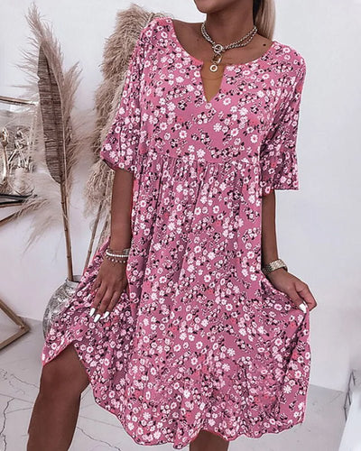 Robe rose à fleurs blanches et noires, manches mi-longues, col en V, portée par une femme. Décor avec plantes séchées en arrière-plan.