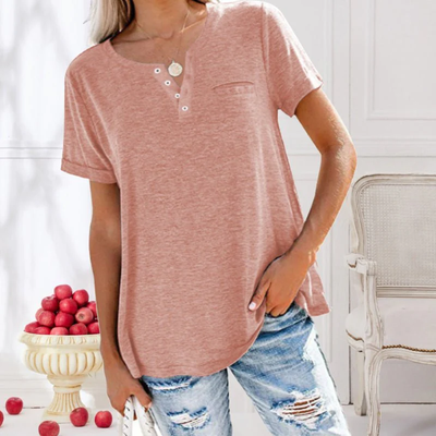 Femme en t-shirt rose, jeans déchirés, posant près d'un vase de pommes rouges. Mode décontractée, intérieur élégant, style estival.