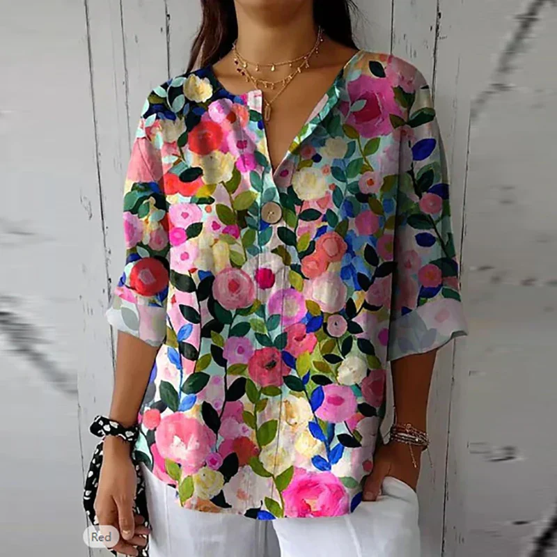 Femme portant une blouse fleurie colorée, manches trois-quarts, sur fond de bois blanc. Mode féminine, tendance printemps-été, style décontracté.
